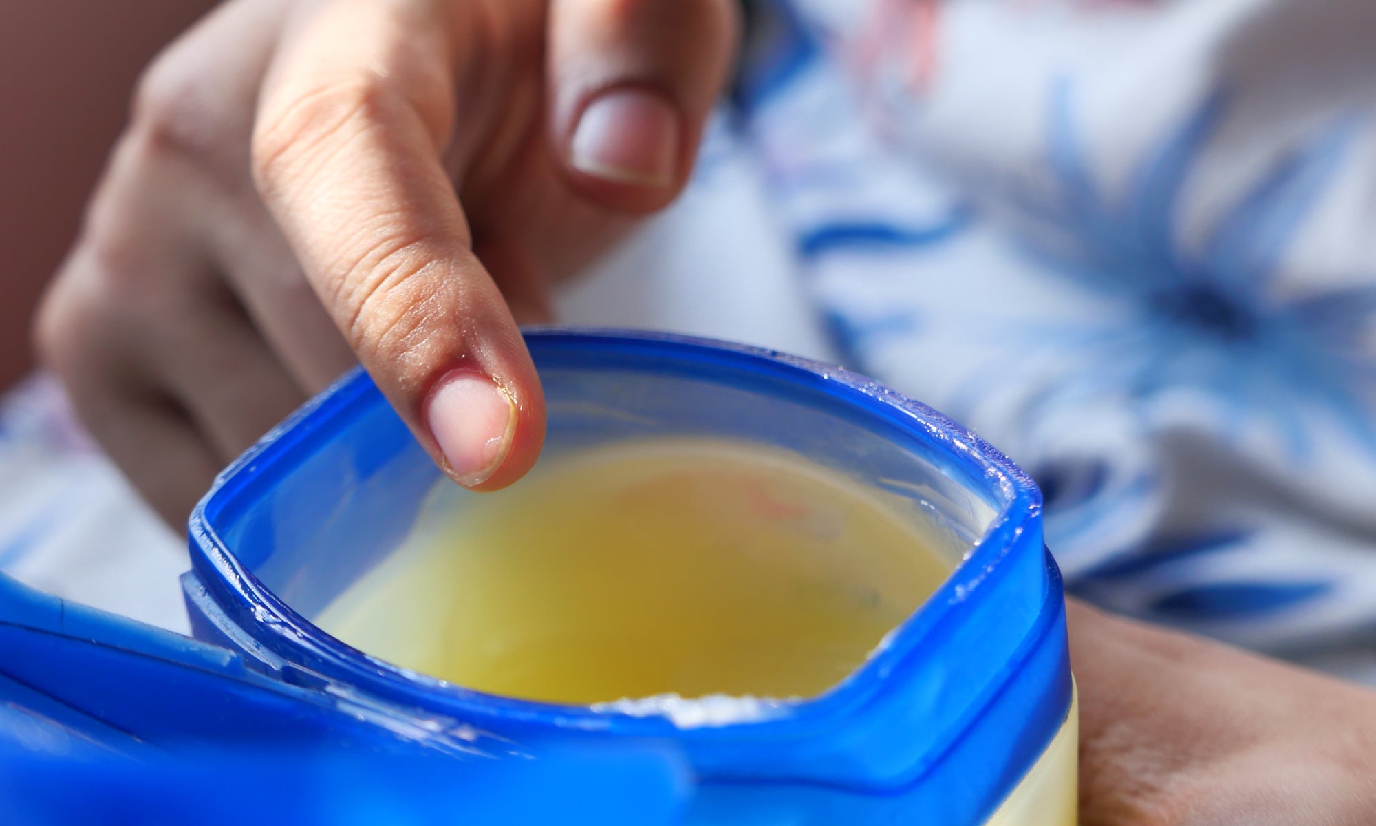 An open plastic pot of Petroleum Jelly with a hand ready to insert a finger into the jelly