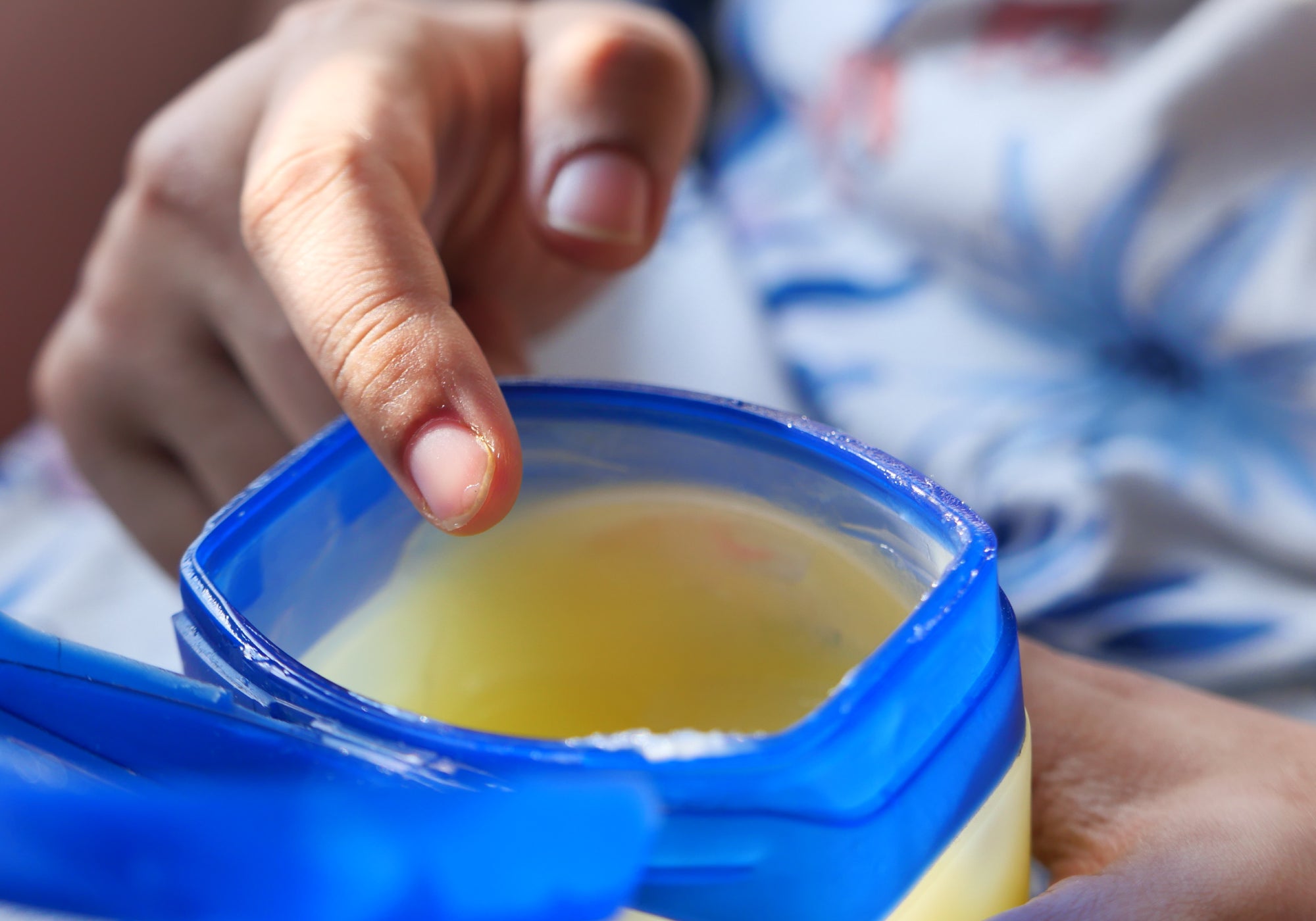 An open plastic pot of Petroleum Jelly with a hand ready to insert a finger into the jelly