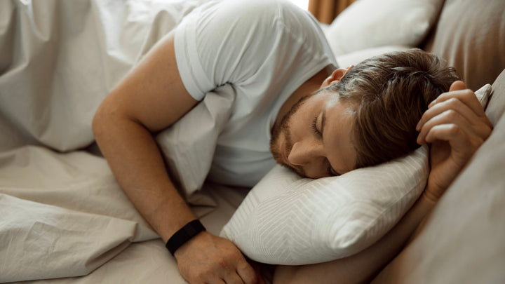 Man sleeping on his side with hand tucked under pillow in white t-shirt and light bedlinen