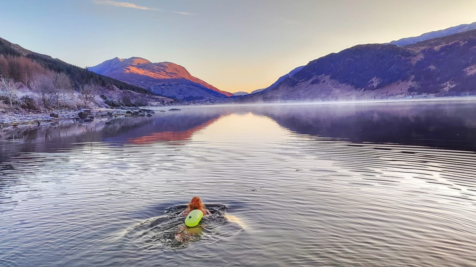 woman floating in wild loch up to the shoulders looking out towards a mountainous range